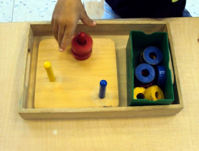 child working with 3 coloured dowels with small rings