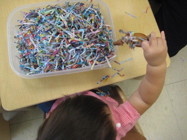 Child under 2 holding an animal and shredded paper 