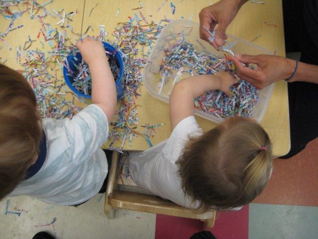 Children under 2 and teacher exploring shredded paper