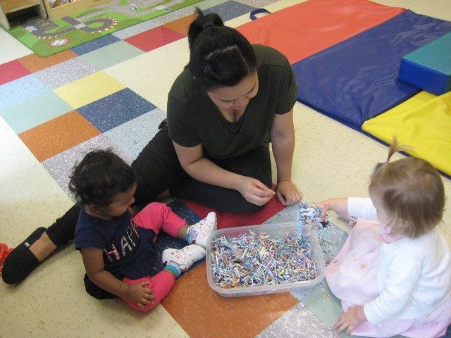 Children under 2 and teacher exploring shredded paper 