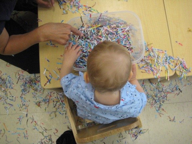 Child under 2 and teacher exploring shredded paper 
