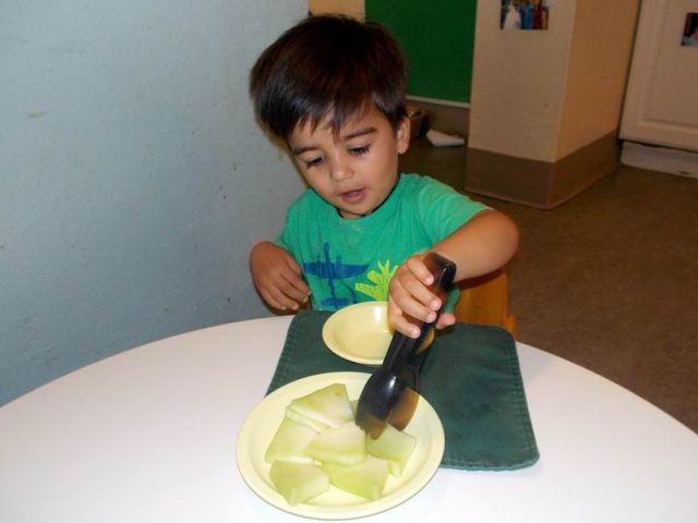 Child under 2 using tongs to serve himself fruit