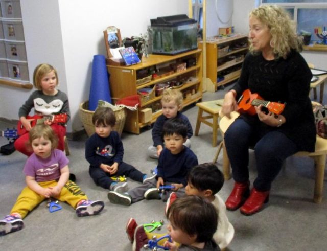 Adrianna playing the ukulele with children observing