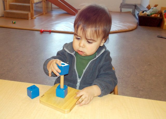 Child under 2 placing a cube on a dowel