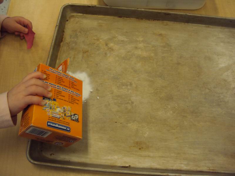 A child's hand pouring baking soda onto a pan