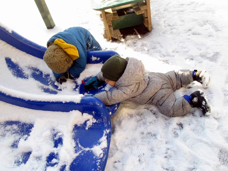 Children observing and wiping snow off the slide