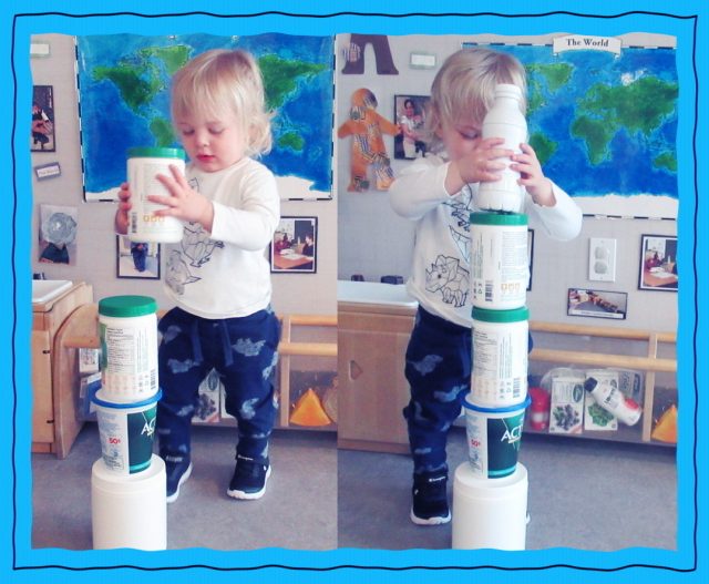 Child under 2 building a tower using recyclable containers.