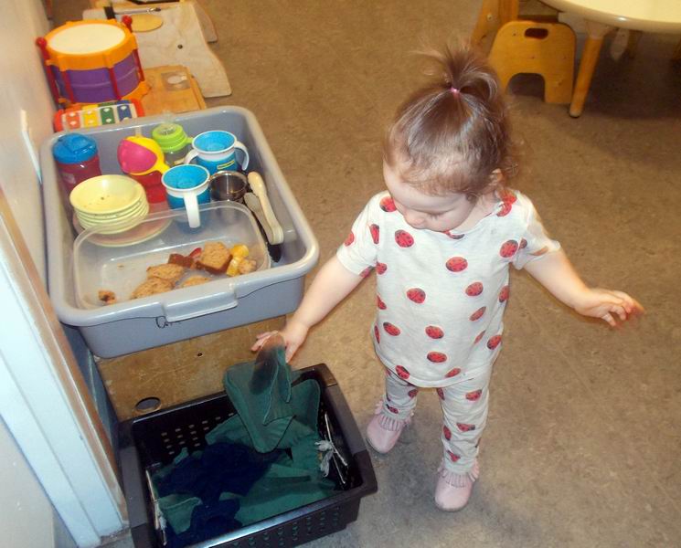 Child under 2 putting a placemat into a laundry basket