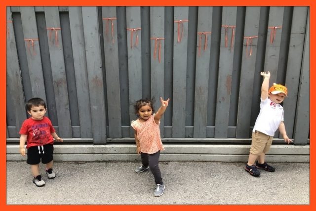 Children under 3 posing in front of fence with orange ribbons