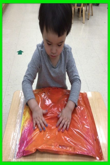 Child under 3 exploring shaving cream and coloured water in a large bag