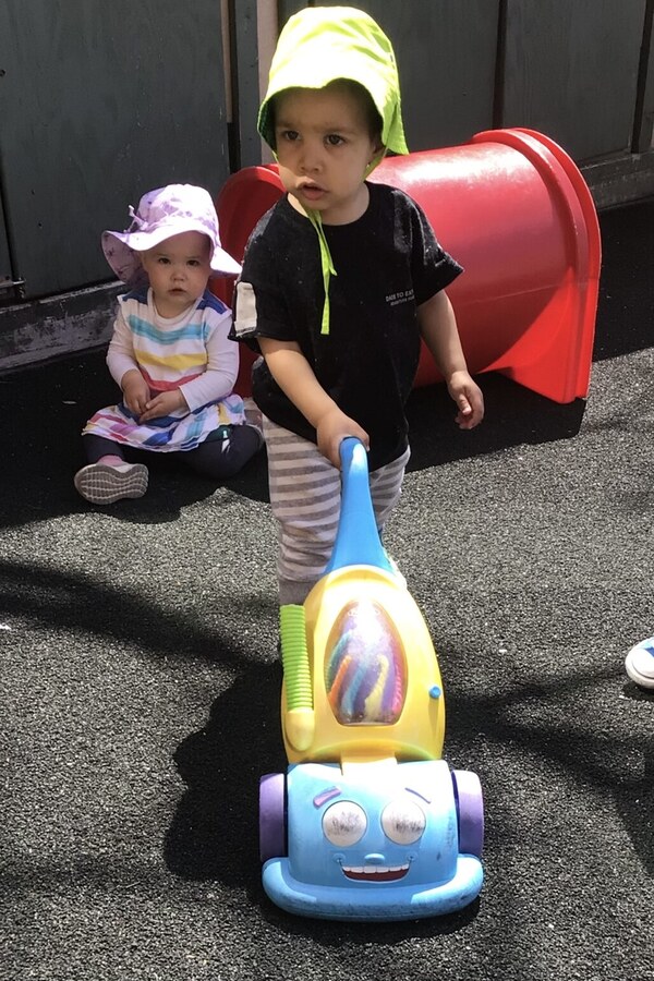 An infant pushing a toy vacuum cleaner