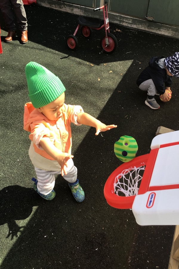 An infant throwing a ball in a basketball net