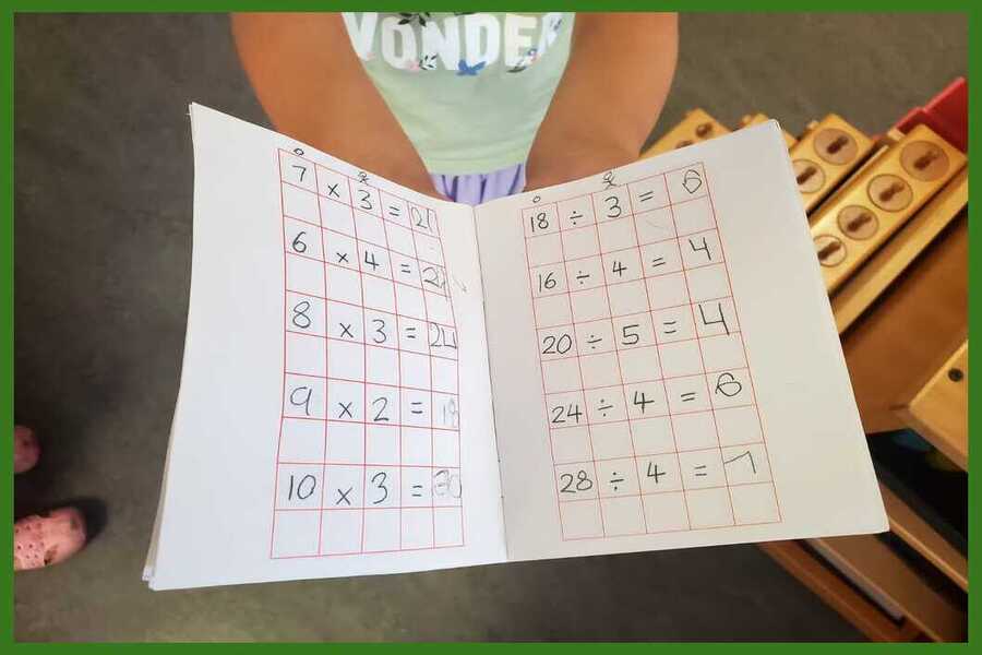 A child showing their math notebook with multiplication and division equations