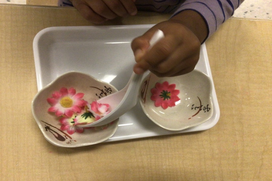 A child spooning objects from bowl to bowl