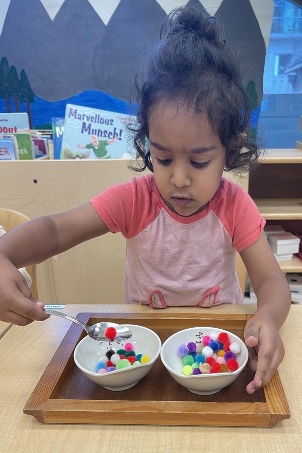 A child spooning pom poms from bowl to bowl