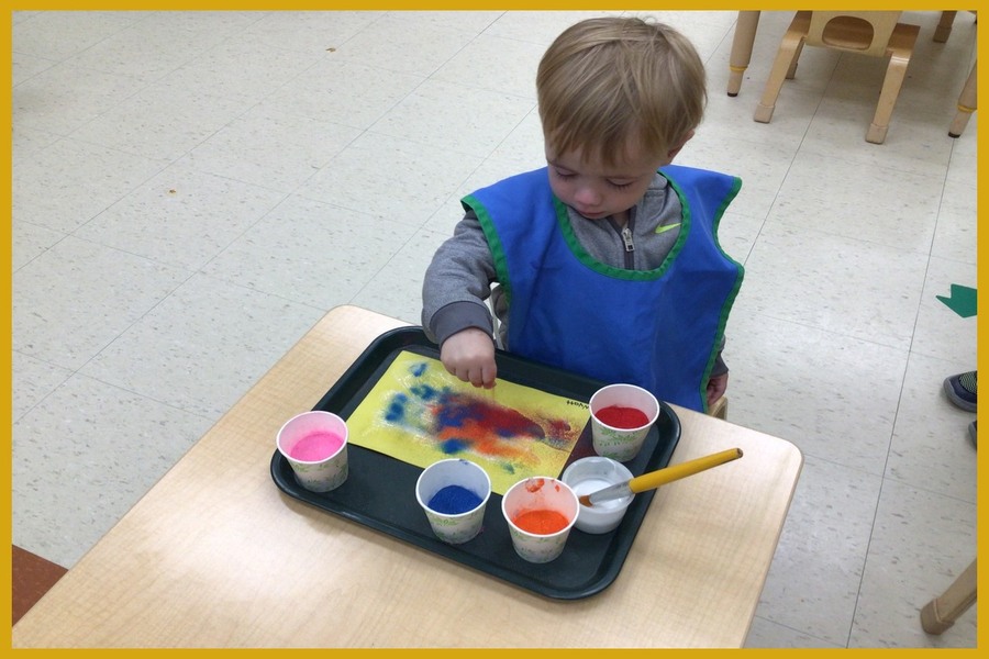 A child sprinkling coloured sand onto glue and construction paper