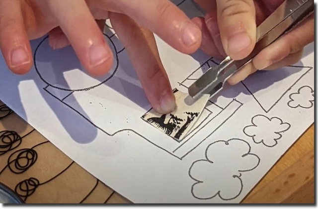 A child placing a collage piece onto a picture with tweezers