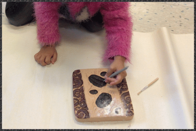 A child using a small tool to uncover a fossil