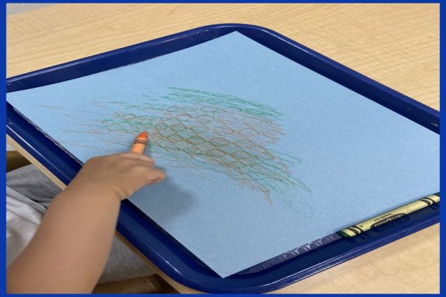 A child colouring with an orange crayon on blue paper