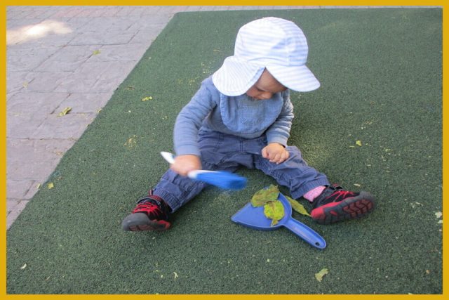 A child sweeping leaves onto a dustpan with a hand broom