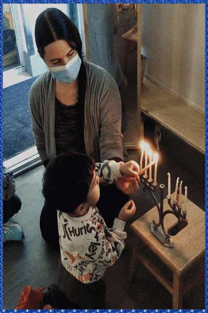 A child and teacher using a shamash to light a candle on a menorah