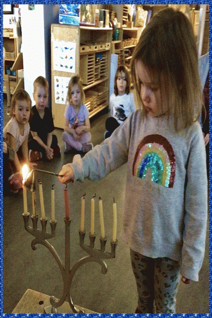 A child snuffing a candle on a menorah with a teacher's assistance