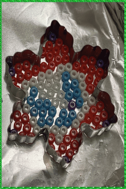 A snowflake metal cookie cutter shape with coloured pony beads placed in a pattern inside
