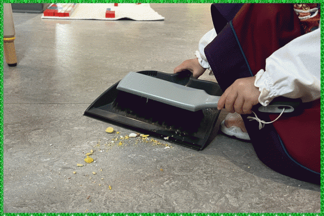 A child using a sweeper and dustpan to clean crumbs off the floor