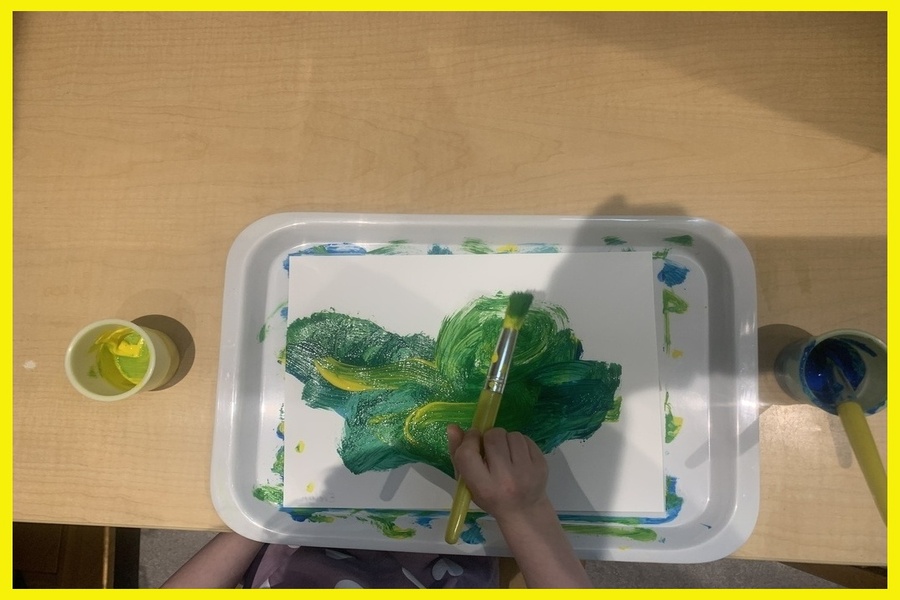 A child painting a white piece of cardstock with green and yellow