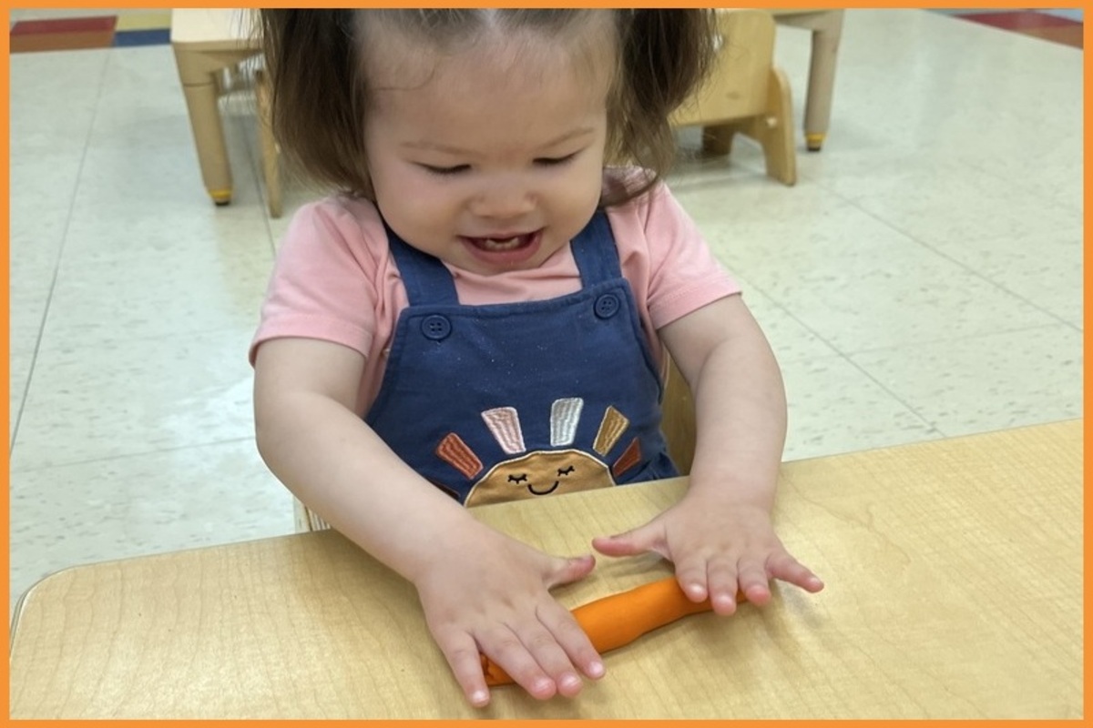 A child rolling orange playdough with her hands