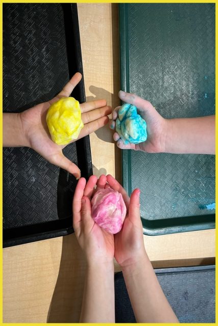 Children holding balls of pink, yellow, and blue playdough