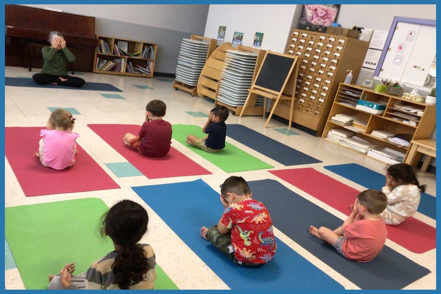 Children doing a 'palming' yoga pose with Cheeba with their hands over their eyes, their fingers touching their forehead, and the heels of their hands resting on their cheeks.