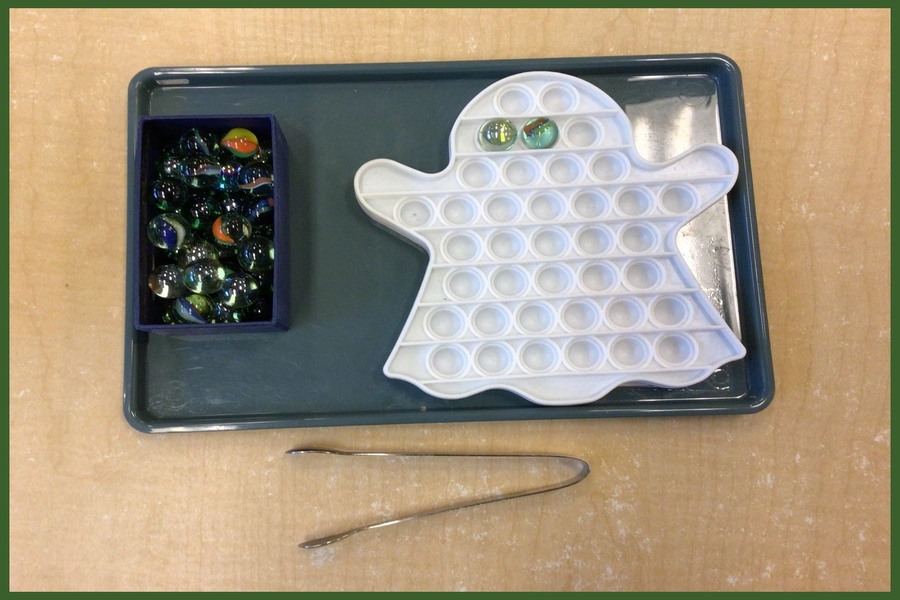 A transferring activity with tongs, marbles, and a ghost shaped dish with indentations to hold the marbles