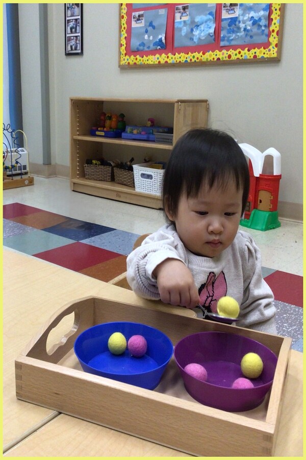 A child spooning pom poms from bowl to bowl