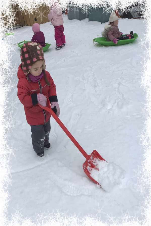 A child shoveling snow with children in sleds in the background