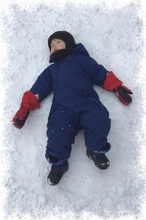 A child laying back in the snow with arms and feet spread like a snow angel