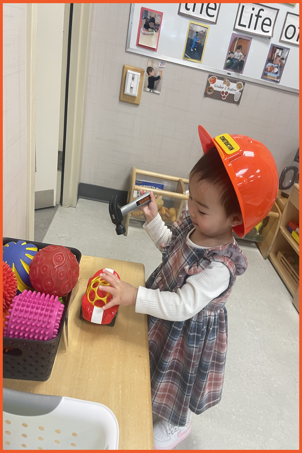 A child wearing a construction hat and holding a hammer and a car