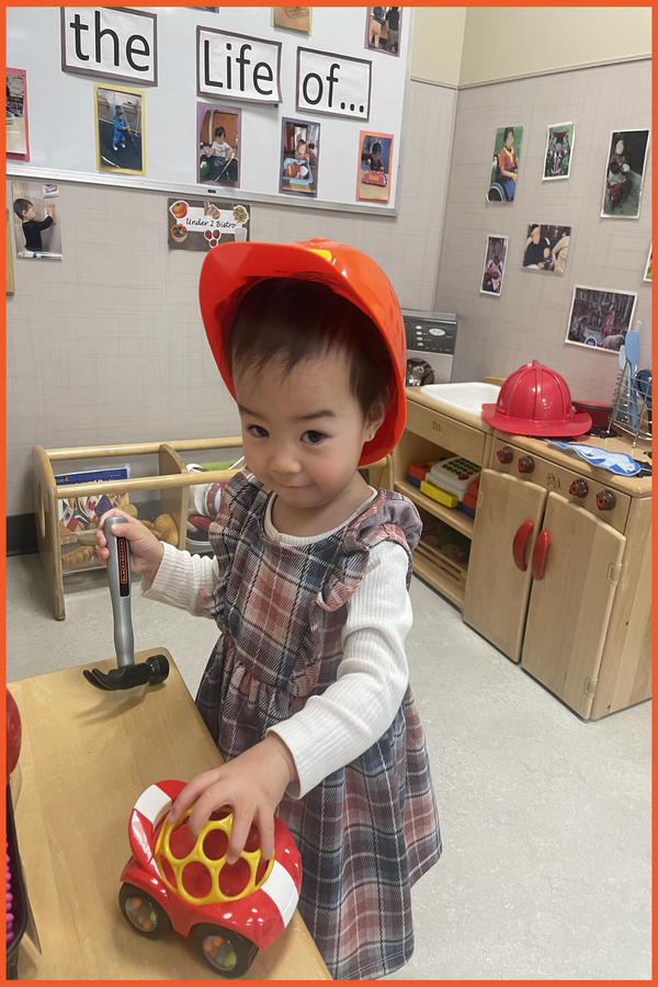 A child wearing a construction hat and holding a hammer and a car