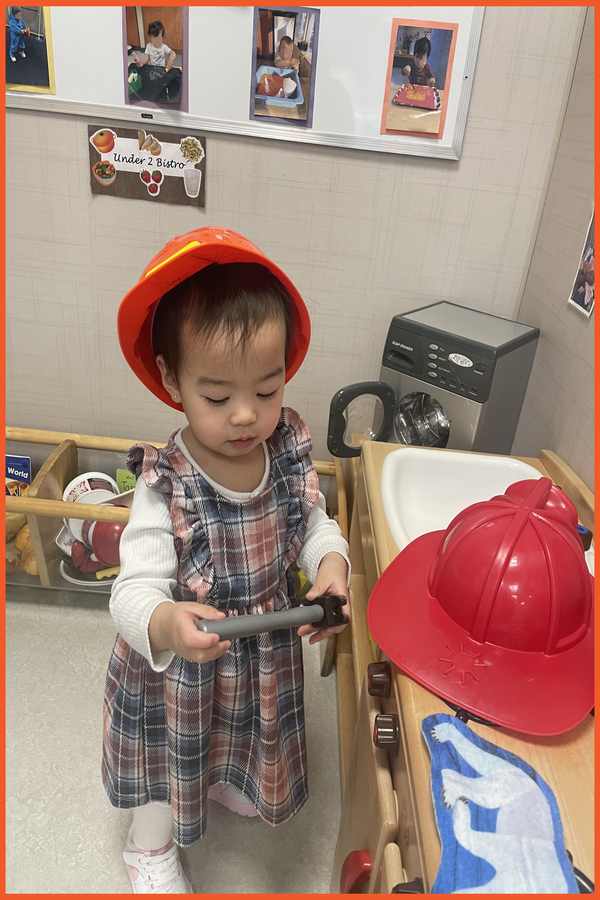 A child wearing a construction hat and holding and examining a hammer